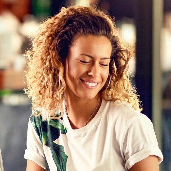 Frau mit Locken sitzt im Restaurant und bestellt lächelnd auf ihrem Smartphone