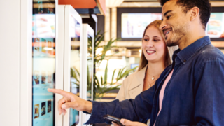 Mann und Frau bedienen lächelnd Self Service Terminal