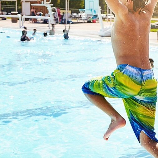 Junge in Badekleidung im Freibad springt in einen Pool.