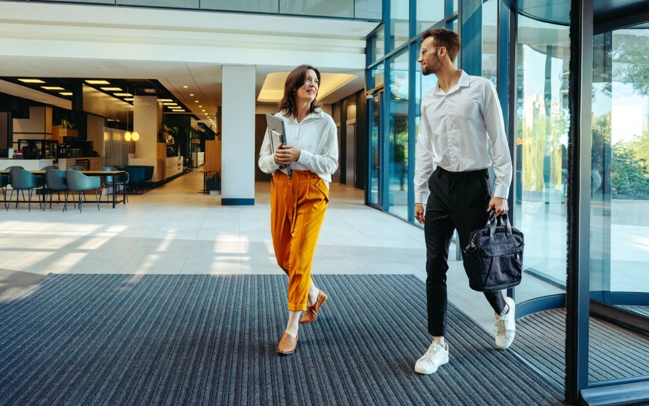 Mann und Frau betreten modernes Bürogebäude