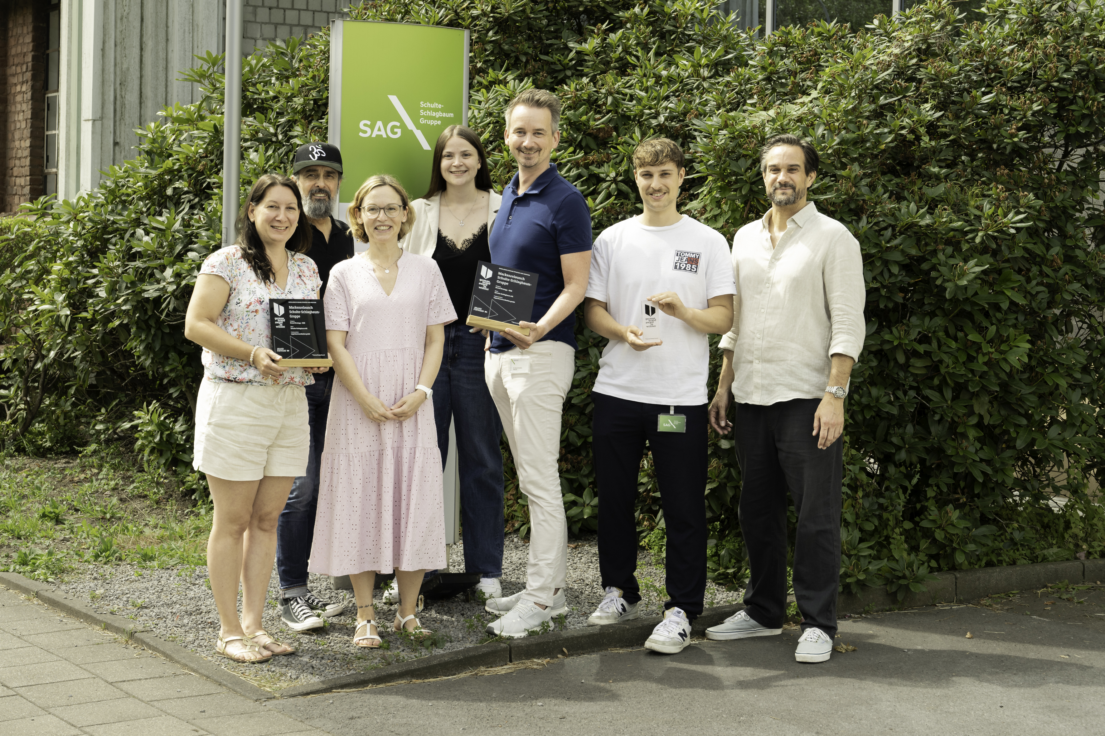 Gruppe von sieben Menschen steht vor einer Stele mit dem Logo der Schulte-Schlagbaum AG. Drei der Menschen halten den German Brand Award in der Hand.
